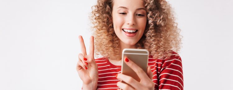 Portrait of cheerful young girl with curly hair waving to mobile phone isolated over white background